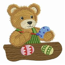 Playful bear in a green shirt painting colorful Easter eggs on a log with a paintbrush and palette.