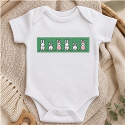 Playful bunny rabbits in pink and white featured on a white onesie against a vibrant green background for Easter.