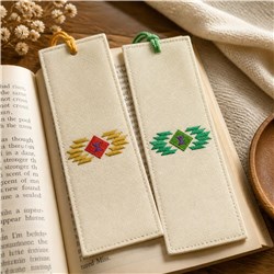 Two geometric bookmarks in light fabric with diamond designs in red, yellow, and green, displayed on a book.