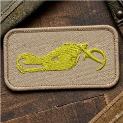 Stylized yellow fish on beige patch, simple minimalist embroidery style, set against wooden background.