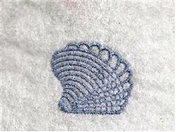 Elegant embroidered seashell in blue thread with fine layered lines, set against a textured white background.