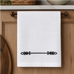 Decorative scroll towel with a minimalistic black scroll design on a white fabric, set against warm wood.