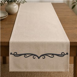 Elegant beige table runner on a wooden table, featuring dark decorative embroidery at the ends.