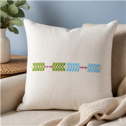 Cream decorative pillow featuring modern embroidered green and blue leaves with red accents on a light sofa.