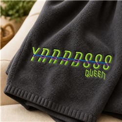 Modern fleece towel featuring vibrant green and purple embroidery on dark grey fabric, showcasing intricate text design.