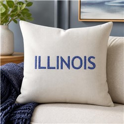 Cream throw pillow with blue embroidered 'ILLINOIS', modern clean style on a cozy sofa.
