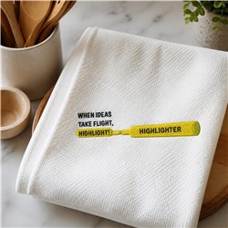 Kitchen towel with playful text 'WHEN IDEAS TAKE FLIGHT, HIGHLIGHT!' and a bright yellow highlighter illustration.