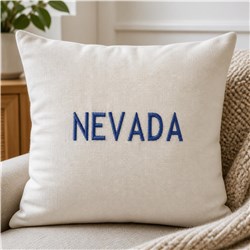 Modern decorative pillow with bold blue 'NEVADA' text on cream fabric, enhancing a cozy interior setting.