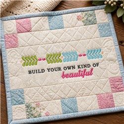 Quilted fabric panel featuring pastel square patches and lively text, enhanced by leaf designs and a cozy, playful look.