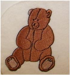 Cartoon teddy bear with lighter accents sits on soft cream fabric background, showcasing playful embroidered stitching.
