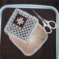 Intricate embroidered patch featuring geometric patterns in black, white, and pink on textured fabric, with scissors nearby.