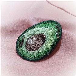 FSL avocado slice with rich green tones, a brown pit, and vibrant embroidered detail on soft pink fabric.