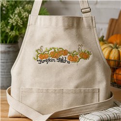 Beige apron adorned with colorful pumpkins and green vines, featuring whimsical 'Pumpkin Patch' text. Perfect for fall.