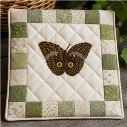 Realistic butterfly with detailed browns and yellows, framed by green and beige patchwork on a quilted background.