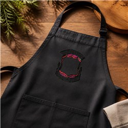Black apron with elegant pink and black embroidery, featuring a warm wooden background for everyday kitchen use.