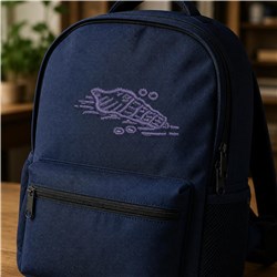 Navy backpack features an elegant purplish shell applique, set in a cozy indoor space with natural light.