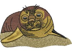 Cute seal head with expressive eyes, resting on sandy surface, featuring colorful stitching in warm tones.