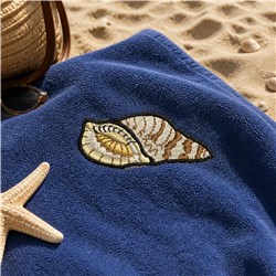 Realistic seashell embroidery on a blue beach towel, surrounded by a starfish and sunglasses on sandy summer shore.