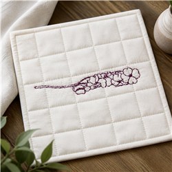 Redwork flower branch on a quilted pot holder against a soft beige background, featuring maroon embroidery and textured fabri