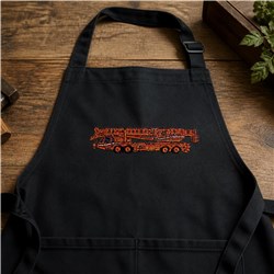 Applique fire truck on a black apron with vibrant orange threads, set against rustic wood.