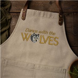 Rustic beige apron featuring a wolf illustration and bright yellow text 'Dance with the WOLVES', styled with leather straps.