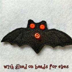 Whimsical bat made from black fabric with pronounced wings and orange bead eyes, perfect for Halloween decor.