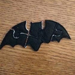 Playful black bat applique in puzzle shape on wood, perfect for Halloween-themed decor.