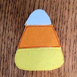 Playful candy corn in applique style with a blue top, orange middle, and yellow base against a rustic wooden backdrop.