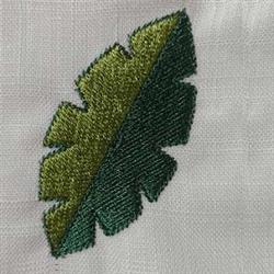 Realistic embroidered green leaf with intricate vein detailing on light fabric, perfect for nature themes.