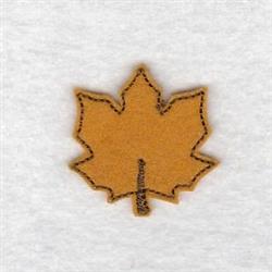 Stylized maple leaf in warm yellow-brown with dark outline stitching, perfect for fall-themed projects.