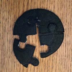 Black puzzle piece with interlocking edges, simplistic and playful style, set against a wooden background.